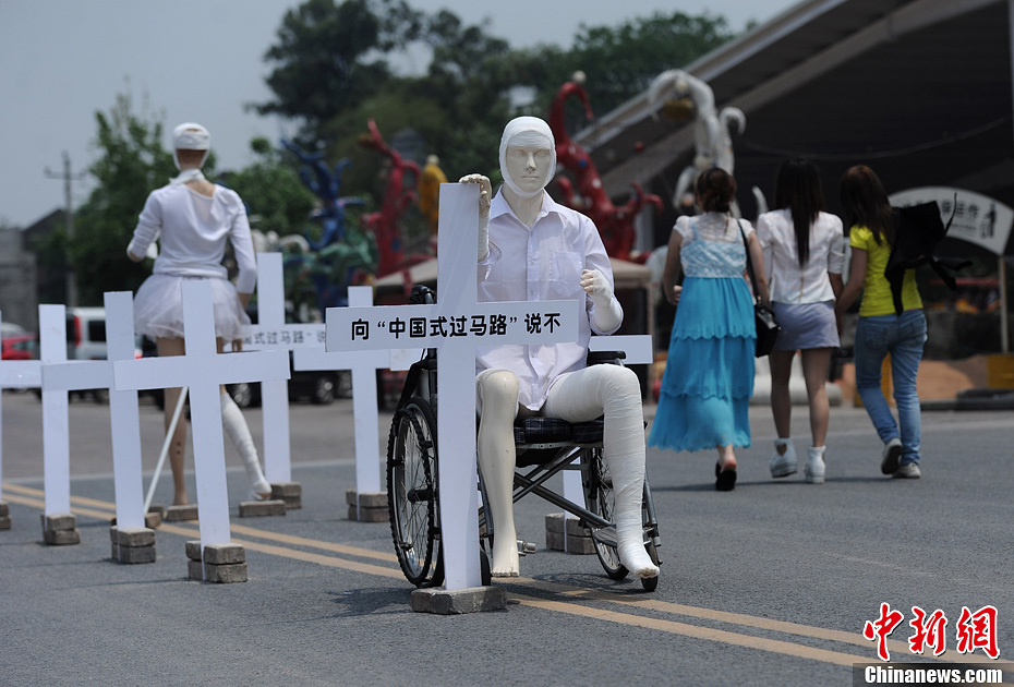4月16日，重慶市洋人街上擺放著兩個受了傷的塑料人像“模特”，旁邊十字架上寫著向“中國式過馬路”說不