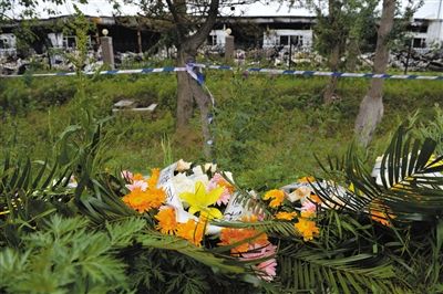 昨日，吉林省德惠市吉林寶源豐禽業(yè)有限公司燃燒事故現場警戒線外，遇難者家屬在路邊擺放了花圈祭奠逝去的親人。吳江 攝